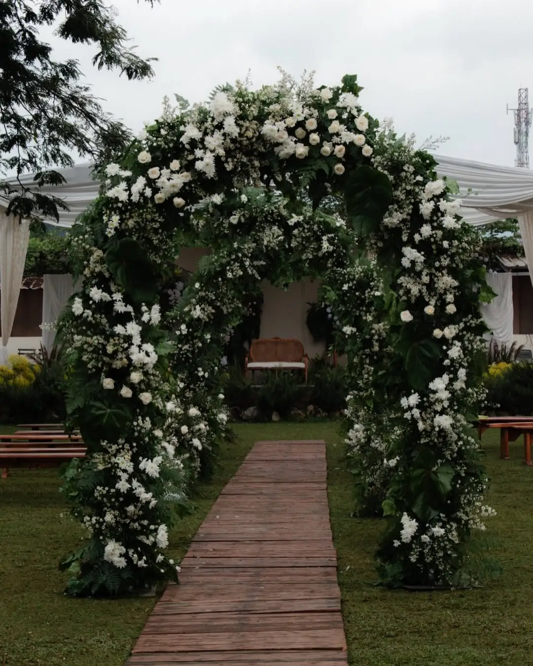 A floral arch over a wooden walkway leading into the garden